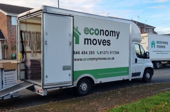 An economy moves van with doors open, loading boxes into the back of the van